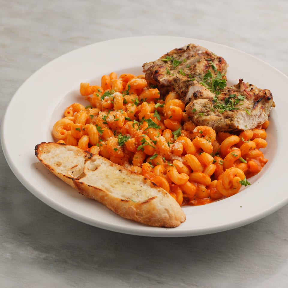 Grilled chicken and cavatappi pasta in red sauce, garnished with parsley and a side of garlic bread.